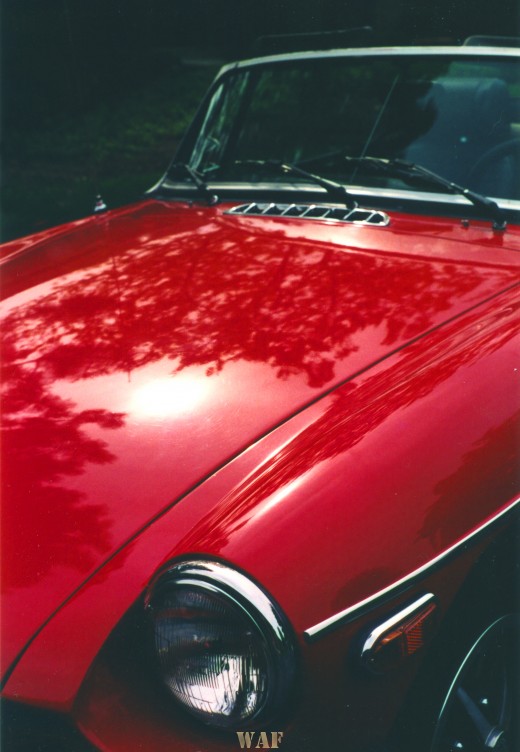 a "postcard corner" of the hood and front of a red MG Anniversary Edition convertible